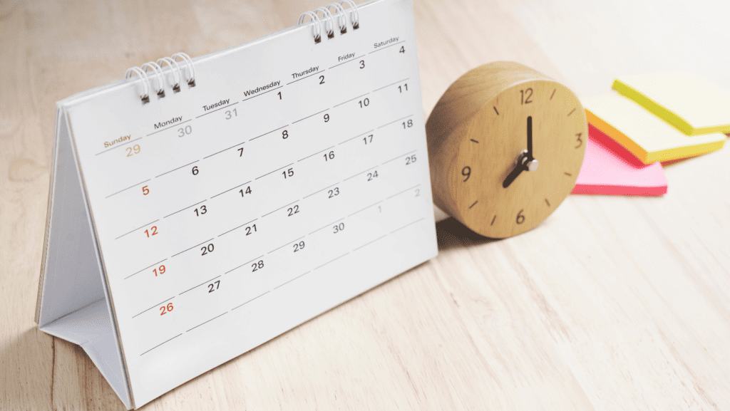 Table with a paper calendar and wood clock and post its to describe calendar management