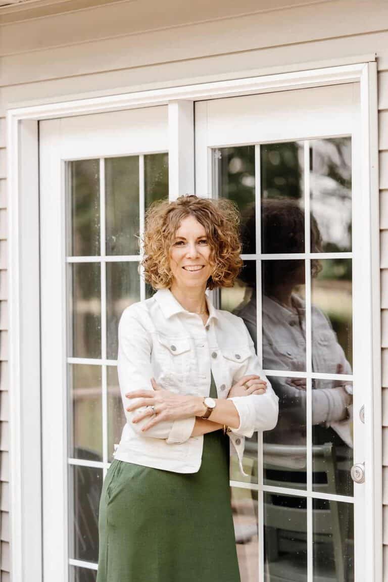 Woman standing by French Doors thinking about the types of motivation and how they influence our habits.