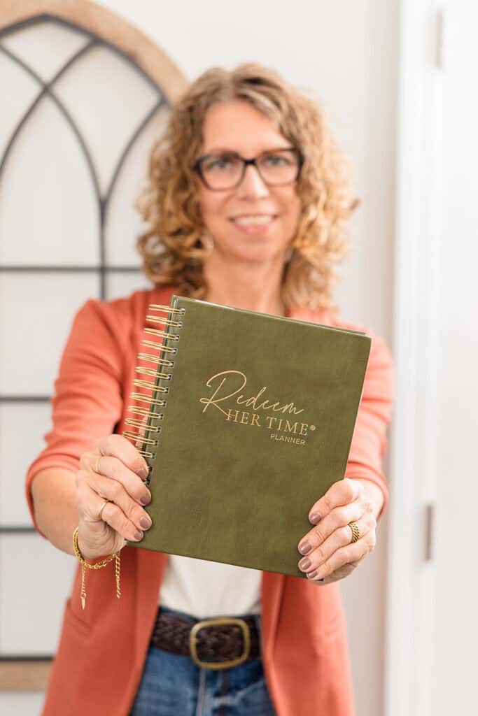 A lady holding the Redeem Her Time Planner to start stewarding her time.