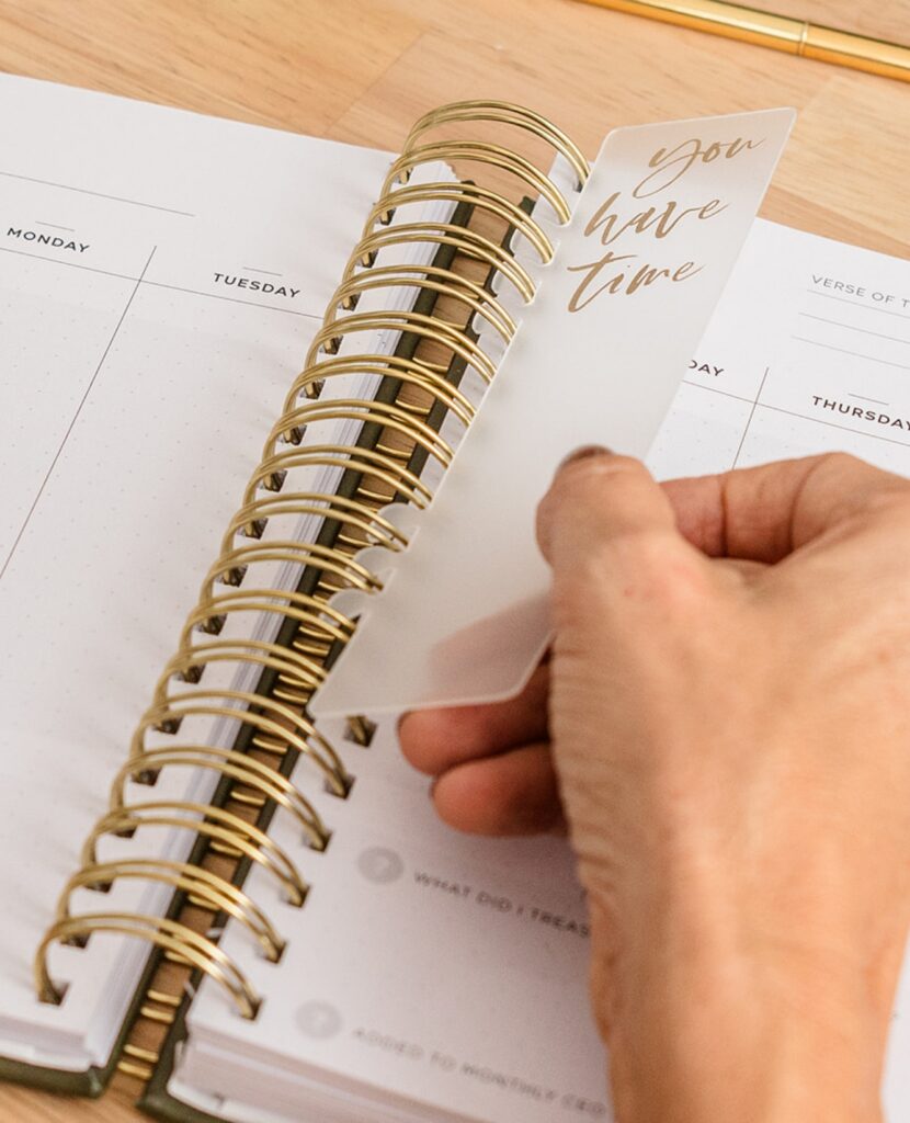 Hand placing a 'You have time' bookmark into the Redeem Her Time Planner — encouragement for Christian women to plan with purpose