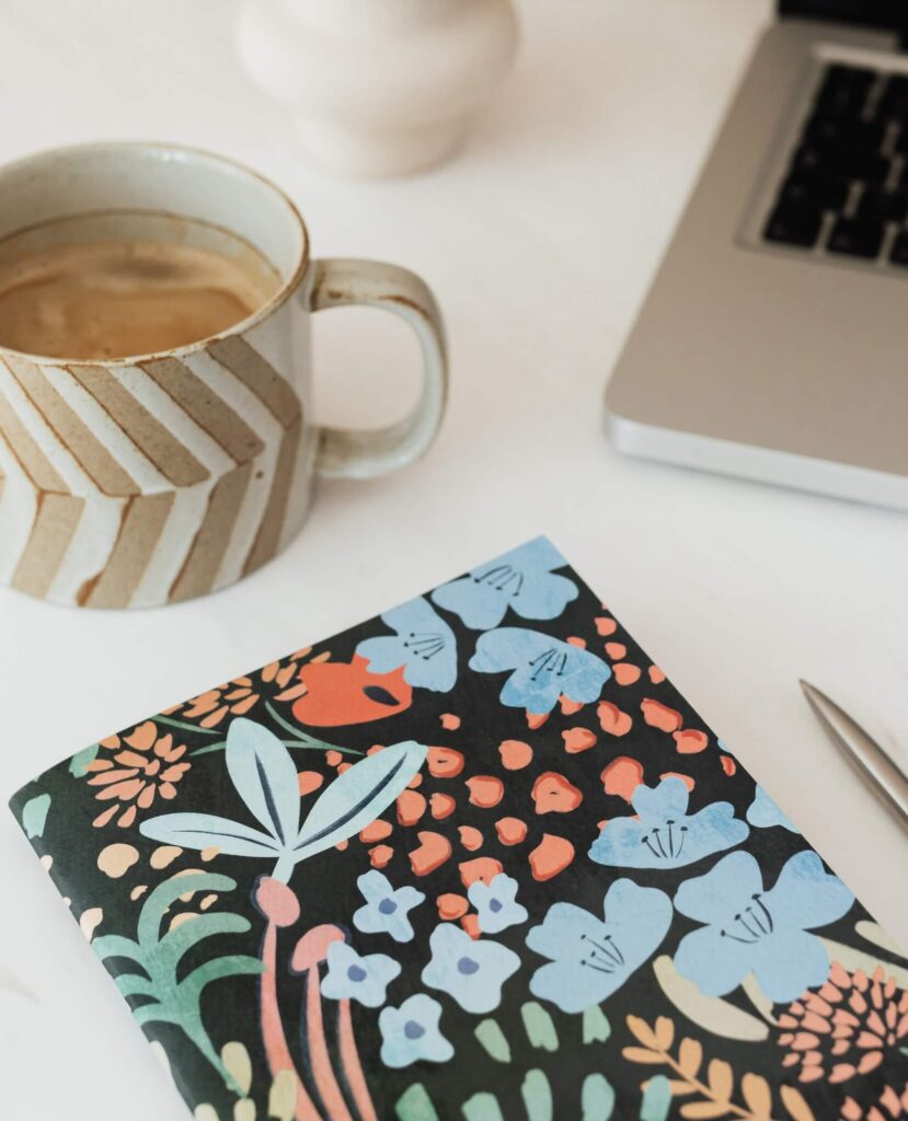 Colorful floral journal next to a coffee mug and laptop—Christian time management course workspace setup