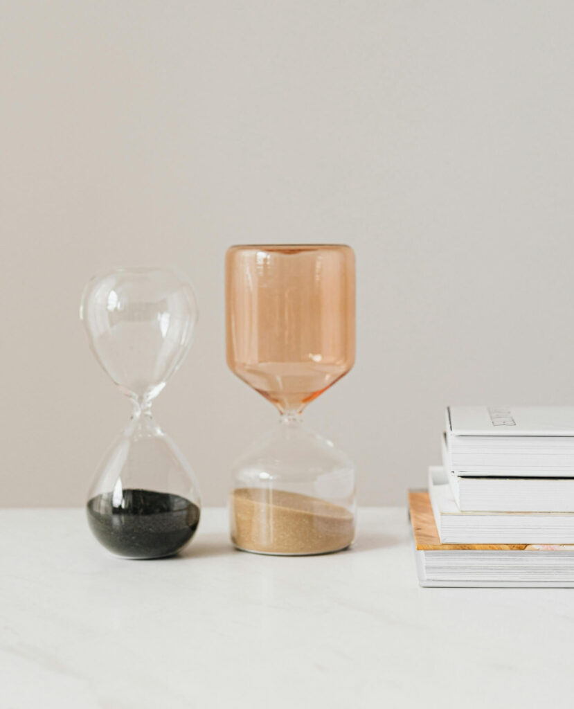 Two modern hourglasses and a stack of books on a white desk—visual metaphor for a time management program