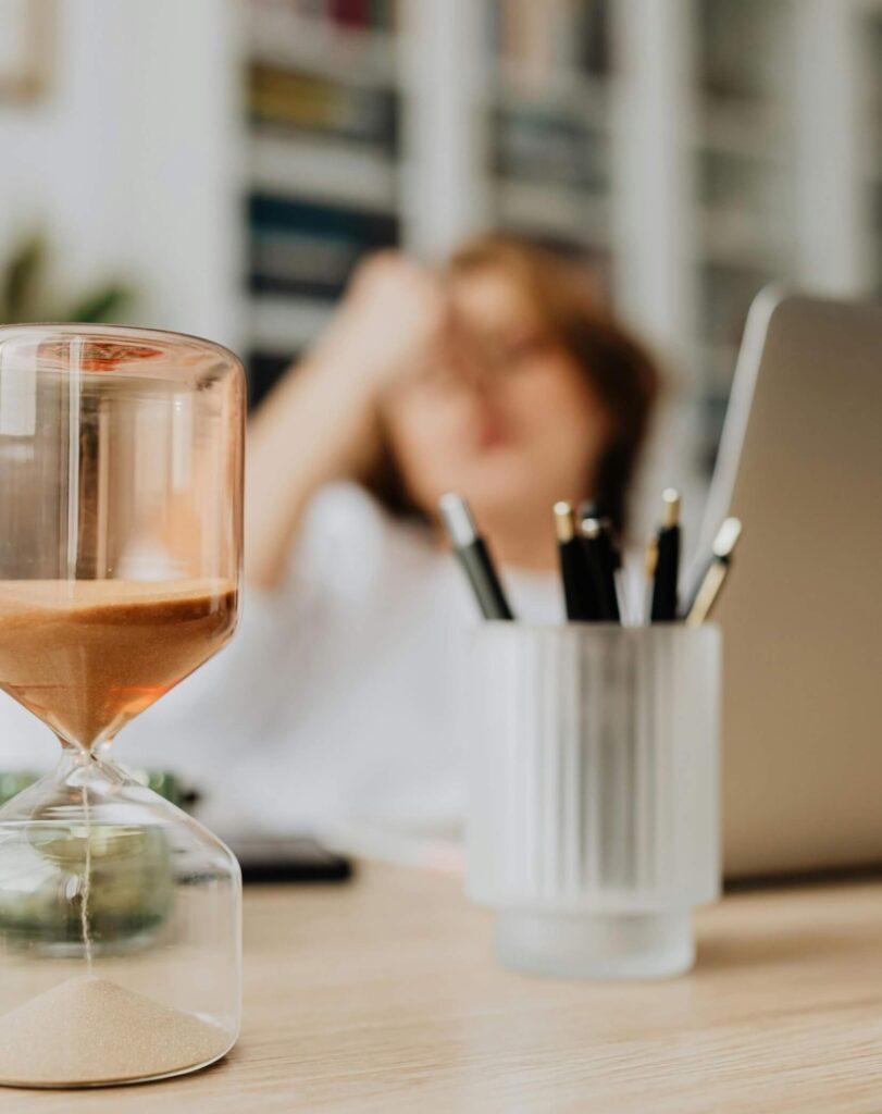 Glass hourglass and black pens organized in containers on a modern office desk