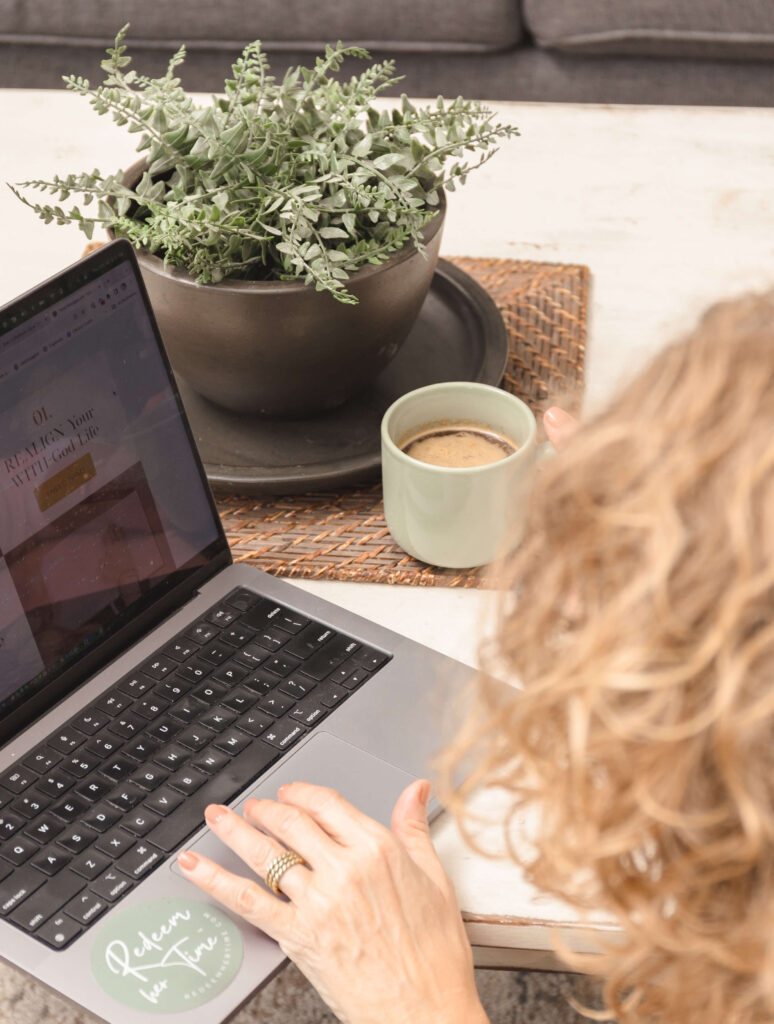 Woman working on laptop with coffee and plant on desk